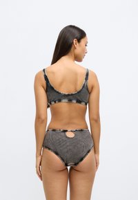 Μαύρο μπικίνι tie-dye με ανοιχτή πλάτη και ψηλόμεσα εσώρουχα. Διαθέτει κυκλικό άνοιγμα στο πίσω μέρος και λεπτομέρειες αντίθετης ραφής.