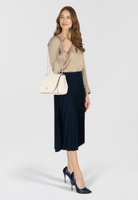 Blusa beige, gonna plissettata blu navy, borsa crema con bordi neri e scarpe con tacco blu navy. Linee pulite, trame lisce e dettagli discreti.