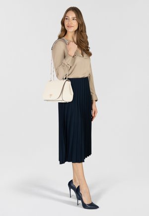 Blusa beige, gonna plissettata blu navy, borsa crema con bordi neri e scarpe con tacco blu navy. Linee pulite, trame lisce e dettagli discreti.