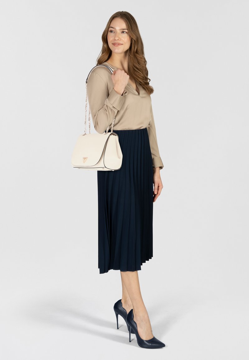 Blusa beige, gonna plissettata blu navy, borsa crema con bordi neri e scarpe con tacco blu navy. Linee pulite, trame lisce e dettagli discreti.