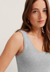 Gray ribbed tank top with wide armholes and a scoop neckline, featuring a soft texture and fitted design. Minimalist style accents.