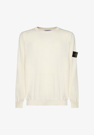 Suéter de manga larga color crema con cuello redondo, puños y dobladillo acanalados, con un parche del logo de Stone Island en negro y amarillo en la manga izquierda.