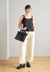 Black satin tank top with shoulder ties, cream wide-leg pants, and black leather platform loafers. Carrying a structured black handbag.