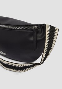 Czarna skórzana torba na ramię o teksturowym wykończeniu, z metalowym zamkiem błyskawicznym i wzorzystym paskiem w kolorze czarnym i kremowym.