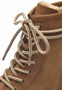 Stivale alla caviglia in pelle marrone con lacci beige, punta arrotondata e morbida fodera in pelliccia. Presenta occhielli metallici e dettagli cuciti.