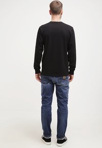 Schwarzes Langarmshirt mit Rundhalsausschnitt, kombiniert mit blauen Jeans aus Denim. Die Jeans haben eine verblasste Waschung und eine detaillierte Rückentaschennaht.
