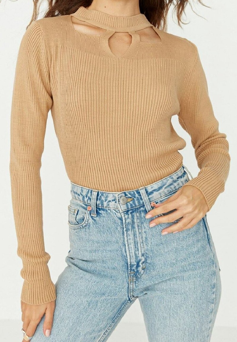 Beiger Rippsweater mit einem Schlitz am Ausschnitt, kombiniert mit hoch taillierten hellblauen Jeans. Lange Ärmel mit enganliegenden Bündchen.
