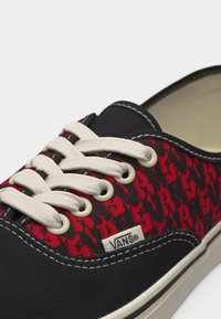 Baskets basses Vans avec lacets blancs, embout noir et tissu rouge à motifs avec des étoiles noires.