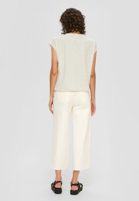 Hellbeige kurzärmliges Oberteil, kombiniert mit hoch taillierten, weit geschnittenen cremefarbenen Hosen. Schwarze Plateausandalen vervollständigen das lässige Outfit.