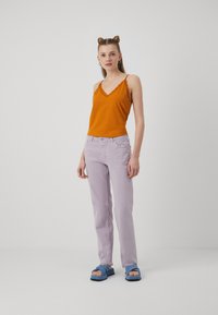 Oransje v-hals tanktopp med teksturert stoff, matchende lavendel rette jeans. Blå sandaler med stroppedesign fullfører antrekket.