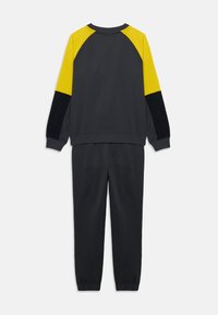Sweatshirt gris et pantalon assorti avec des accents jaunes et noirs. Présente une coupe décontractée, des poignets côtelés et une taille élastiquée.
