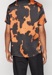 Kurzarmhemd mit glatter, satinierter Textur und abstraktem orange-schwarzen Muster, im lässigen Schnitt gestaltet.