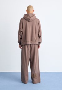 Brun oversized hoodie med snoretræk i hætten, parret med matchende wide-leg sweatpants med en subtil broderet detalje.