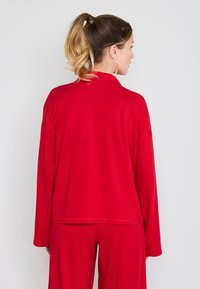 Červený souprava loungewear s dlouhými rukávy, má volný střih. Měkká, hladká textura a jednoduchý design bez ozdob.