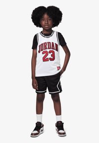 White mesh basketball jersey with red "JORDAN 23" text, paired with black shorts and black sneakers featuring red accents. White socks.