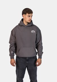 Felpa con cappuccio grigia e tasca frontale, con logo "CRYSTAL" bianco. Tessuto morbido, vestibilità rilassata, polsini e orlo a costine. Indossata con jeans neri.