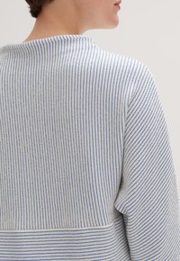 Randig tröja med en texturerad tyg i vitt och blått, med rund halsringning och ett horisontellt randigt band i botten.