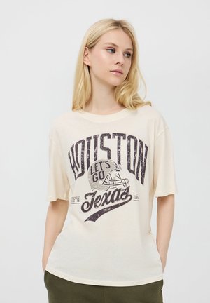 T-shirt a maniche corte color crema con grafica in stile vintage. Presenta il testo "Houston" e "Let's Go Texas" con un design di un casco da football.
