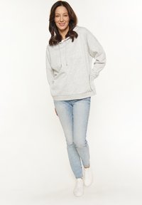 Grauer Kapuzenpullover mit Kordelzug und Kängurutasche, kombiniert mit hellblauen Slim-Fit-Jeans und weißen Sneakern.