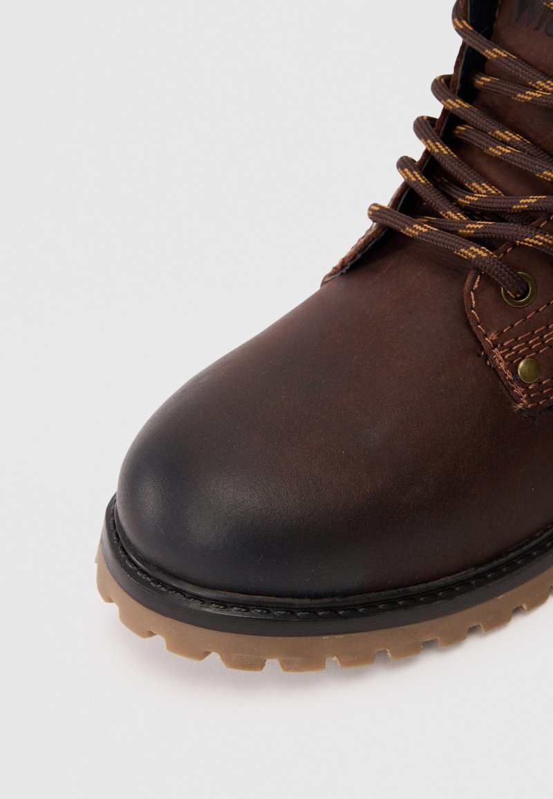 Brauner Lederstiefel mit einer runden Zehenpartie, kontrastierender schwarzer Gummispitze, strukturiertem Schnürdesign und einer hellbraunen, robusten Sohle.