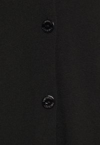 Mustaa neulottua kangasta, jossa on kaksi mustaa nappia, joista kummassakin on kaiverrettuna "TWINSET FESTIVAL" -teksti.