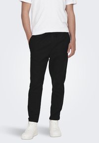 Pantalones negros ajustados hechos de algodón suave con una cinturilla elástica. Combinados con una camiseta blanca y zapatillas blancas.