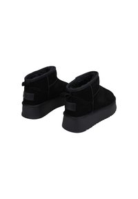 Botas de tobillo de ante negro con un suave forro interior, suela de goma plana y tirador trasero. Presentan un diseño minimalista y sin patrones visibles.