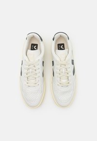 Weiße, durchbrochene Ledersneaker mit navyfarbenen Akzenten und beigen Schnürsenkeln. Merkmale umfassen ein Logo auf der Zunge und eine genoppte Gummisohle.