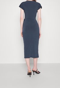 Nauwsluitende midi-jurk in marineblauw van zachte stof, korte mouwen, detail met tailleband, met een recht afgesneden zoom en gedragen met zwarte sandalen met bandjes.