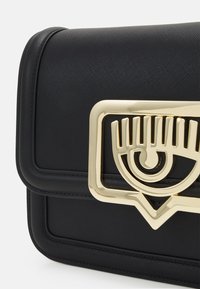 Svart texturerad handväska med en guldögonformad hårdvaruaccent. Har en strukturerad design och en lockstängning med synliga sömmar.