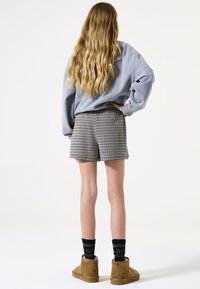 Sudadera gris de gran tamaño, pantalones cortos de cuadro, botas de tobillo de color beige y calcetines negros. La ropa se caracteriza por un ajuste relajado y materiales cómodos.