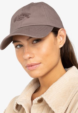 Bruine katoenen baseballpet met geborduurd logo, gebogen rand en stiksels, gedragen met een beige corduroy overhemdjack.