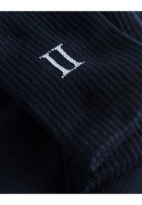 Námornícky modrý pletený materiál s ribovanou textúrou, so žltým vyšívaným logom "II". Materiál vyzerá jemne a elasticky.
