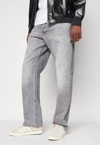 Jeans de denim gris de corte amplio con un desvanecimiento sutil, costuras detalladas y un diseño de pierna recta, combinados con zapatillas ligeras.