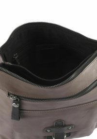 Innenraum einer braunen Ledertasche mit Reißverschluss, schwarzem Stofffutter und einer äußeren Reißverschlusstasche. Verfügt über ein horizontal ausgerichtetes Design und eine strukturierte Oberfläche.