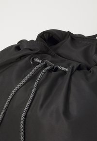 Fekete húzózsinóros táska sima nylon szövetből, kontrasztos szürke fonott zsinórokkal és fekete műanyag zárómechanizmussal.