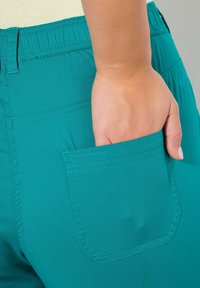 Shorts turchesi con cintura elastica e una tasca posteriore singola. Il tessuto appare liscio con dettagli di cucitura visibili.