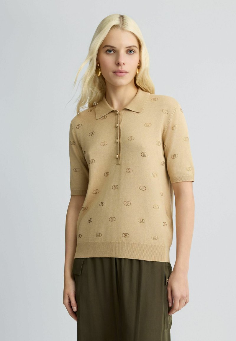 Tan korte mouwen polo trui met een gestructureerd logo patroon, drie knopen en een geribbelde kraag. Gecombineerd met olijfgroene broek.