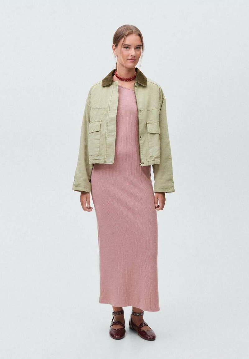 Olive green cropped jacket with large pockets, worn over a ribbed pink maxi dress and brown strap shoes. Neutral background.
