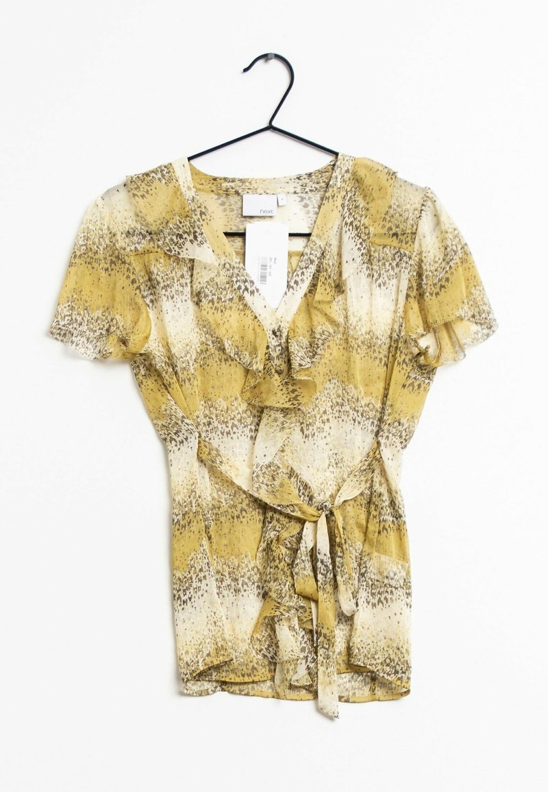 Blouse à motif floral dans des tons jaunes et crème, présentant des manches à volants, un col en V et un lien à la taille. Tissu léger et semi-transparent.