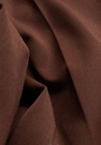 Tessuto di cotone marrone con una texture liscia, caratterizzato da pieghe sovrapposte e una leggera lucentezza, che enfatizza la sua qualità morbida e flessibile.