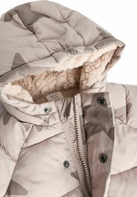 Beige takki, jossa on pehmustettu rakenne, huppu, pehmeä vuori, vetoketjusulku ja hillitty camo-kuvio tummemmissa sävyissä. Sisältää napakkaakkoset.