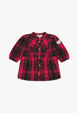 Robe à carreaux rouge et noir avec des manches longues, détail à volants sur le devant et patch d'ours sur la manche gauche. Fermeture à boutons.