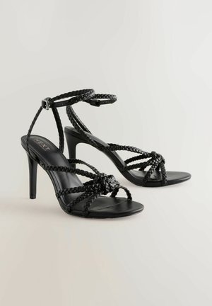 Mustad mustakäised sandaalid punutud rihmadega, kandmisela, ja sileda pinnaga. Avatud varbakujundus koos saleda stilettokannaga.