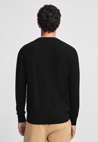 Svart tröja i stickad kvalitet, med ribbade manschetter och nederkant, klassisk rund halsringning och en slät yta.