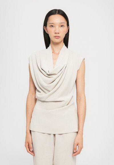 Haut sans manches beige clair avec un col drapé en cowl, fabriqué à partir d'un tissu lisse. Il a une silhouette ajustée et un design propre et minimaliste.