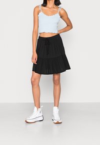 Ljusblått croppat top med vågiga kanter, matchat med en svart lagerkjol och vita höga sneakers. Släta tyger, avslappnad stil.