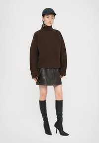 Brauner gestrickter Rollkragenpullover, schwarzer Leder-Minirock, kniehohe schwarze Stiefel mit Absatz, schwarze Kappe, mit Ohrringen und minimalistischer Gestaltung.