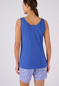 Blauwe mouwloze top met een golvende halslijn, gecombineerd met witte shorts met een blauw loofpatroon. De stof lijkt zacht en lichtgewicht.