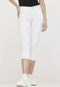 Jean capri blancs en denim extensible, présentant une coupe ajustée, une taille mi-haute et une texture lisse. Assortis à des baskets blanches.
